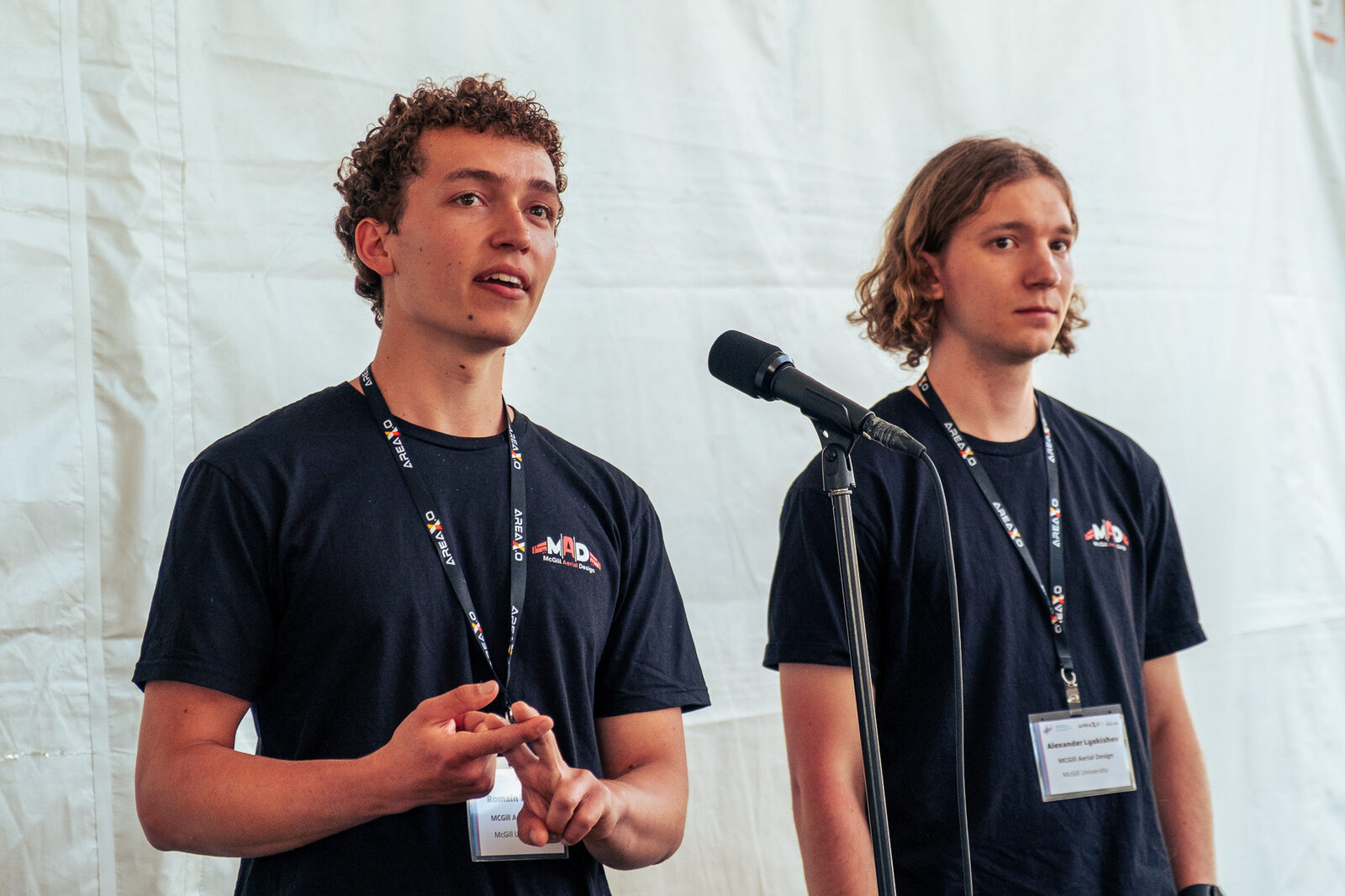 Romain speaking at a microphone alongside a teammate at a competition