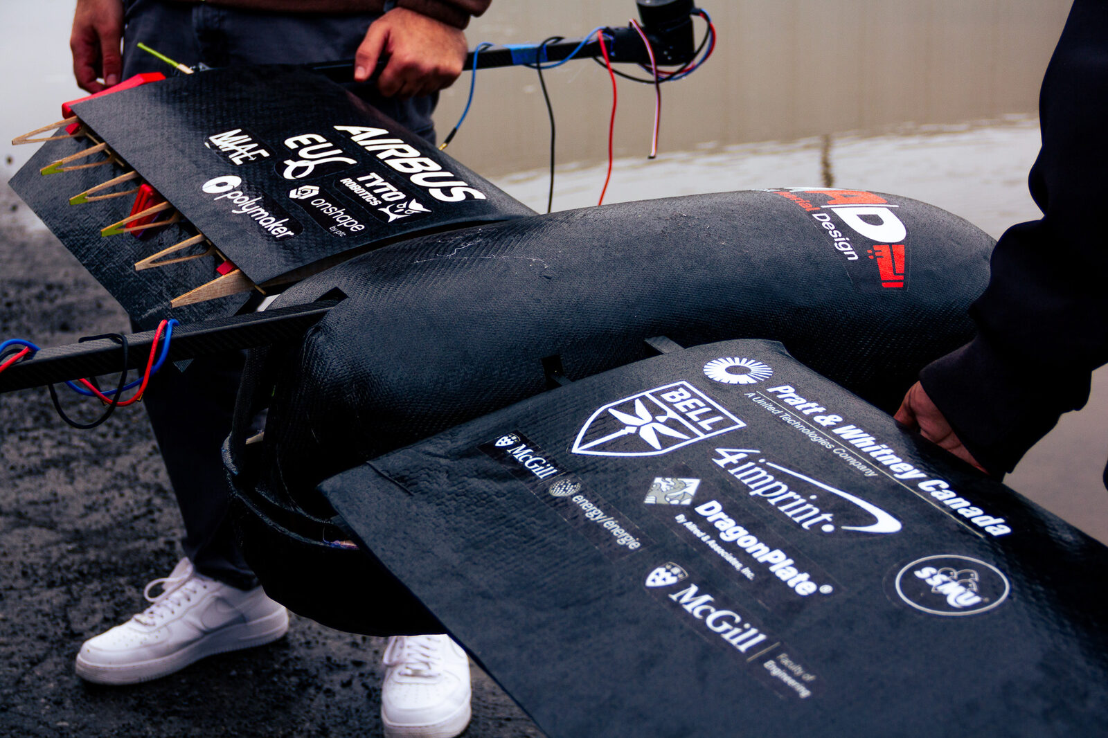 Close-up of a carbon fiber drone wing covered in sponsor logos including Airbus, Bell, and Pratt & Whitney