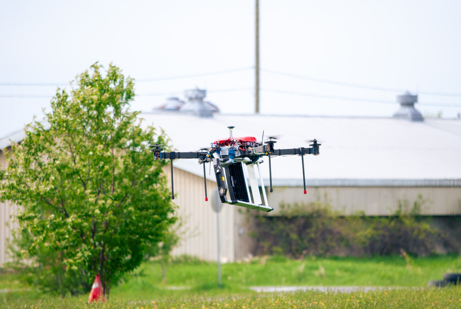 MegaQuad, a large 10.5kg firefighting competition drone, in flight near a tree and building