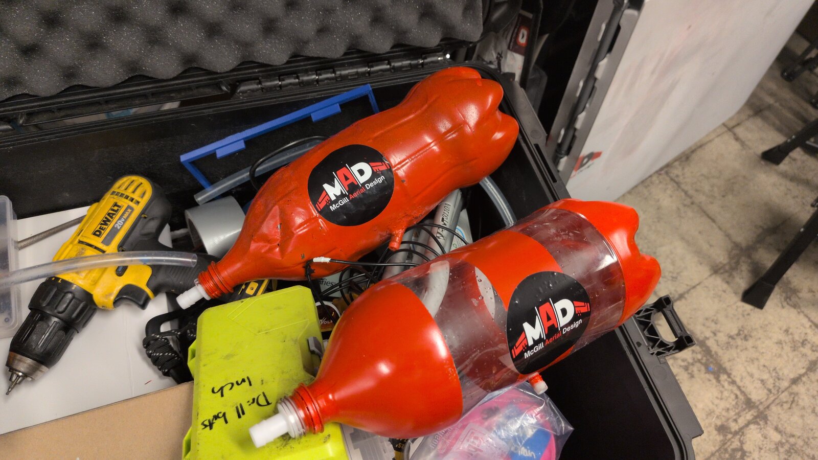 Two red spray-painted 2L soda bottle water payloads with McGill Aerial Design stickers, sitting in a tool case