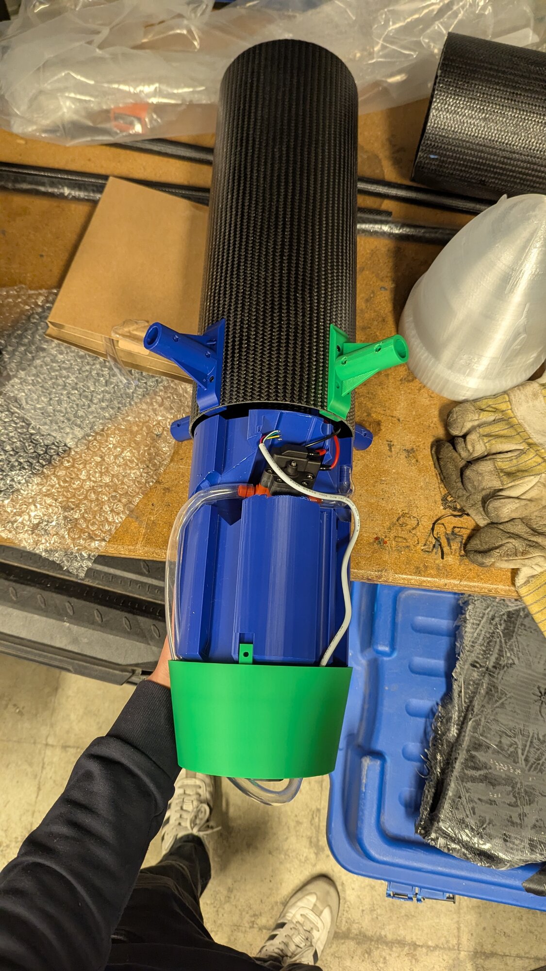 Assembled water payload tank, blue 3D printed body with a carbon fiber nose cap and green mounting ring, held up for a top-down view