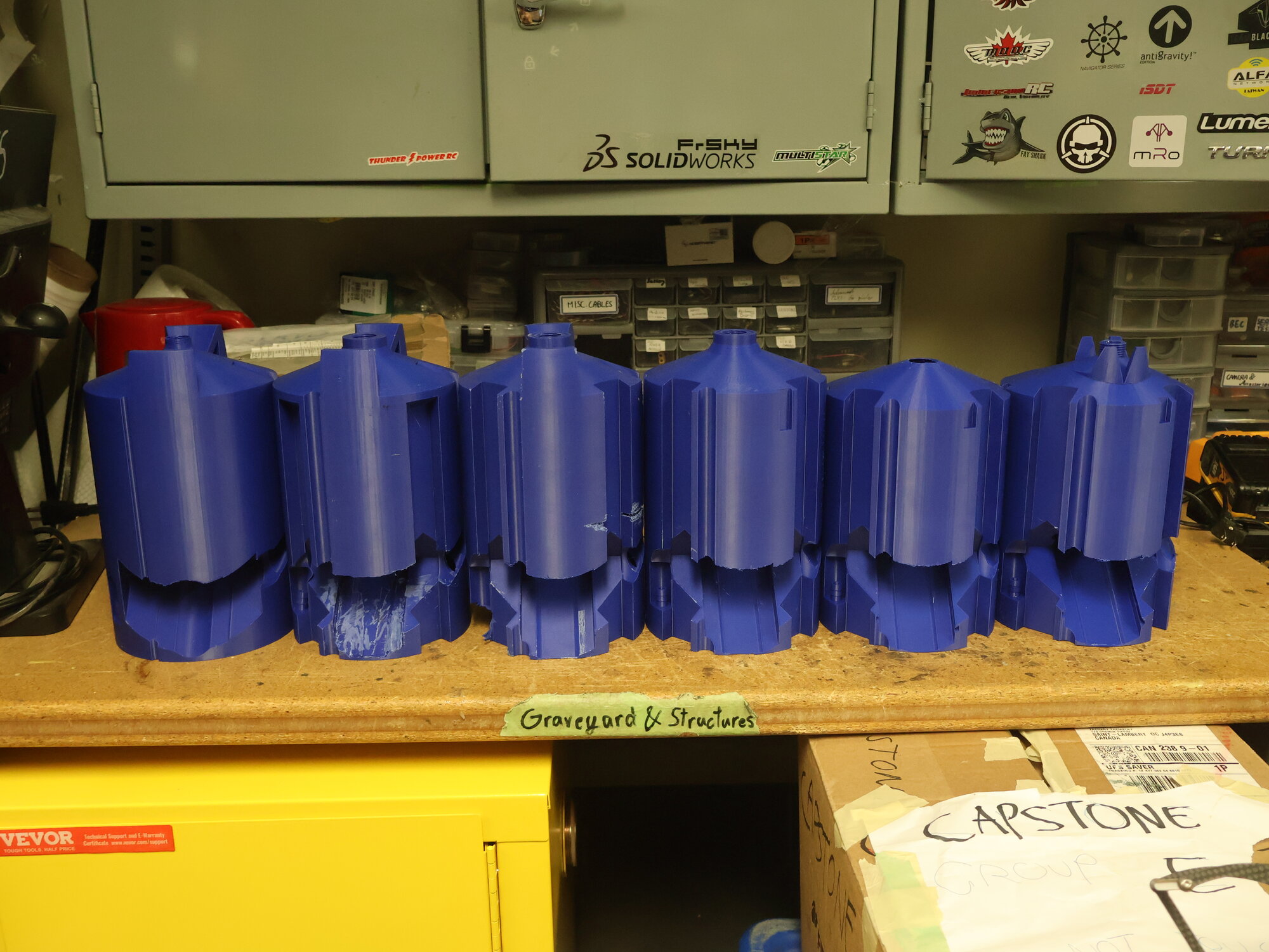 Six generations of 3D printed payload tank prototypes lined up on a shelf labeled Graveyard and Structures