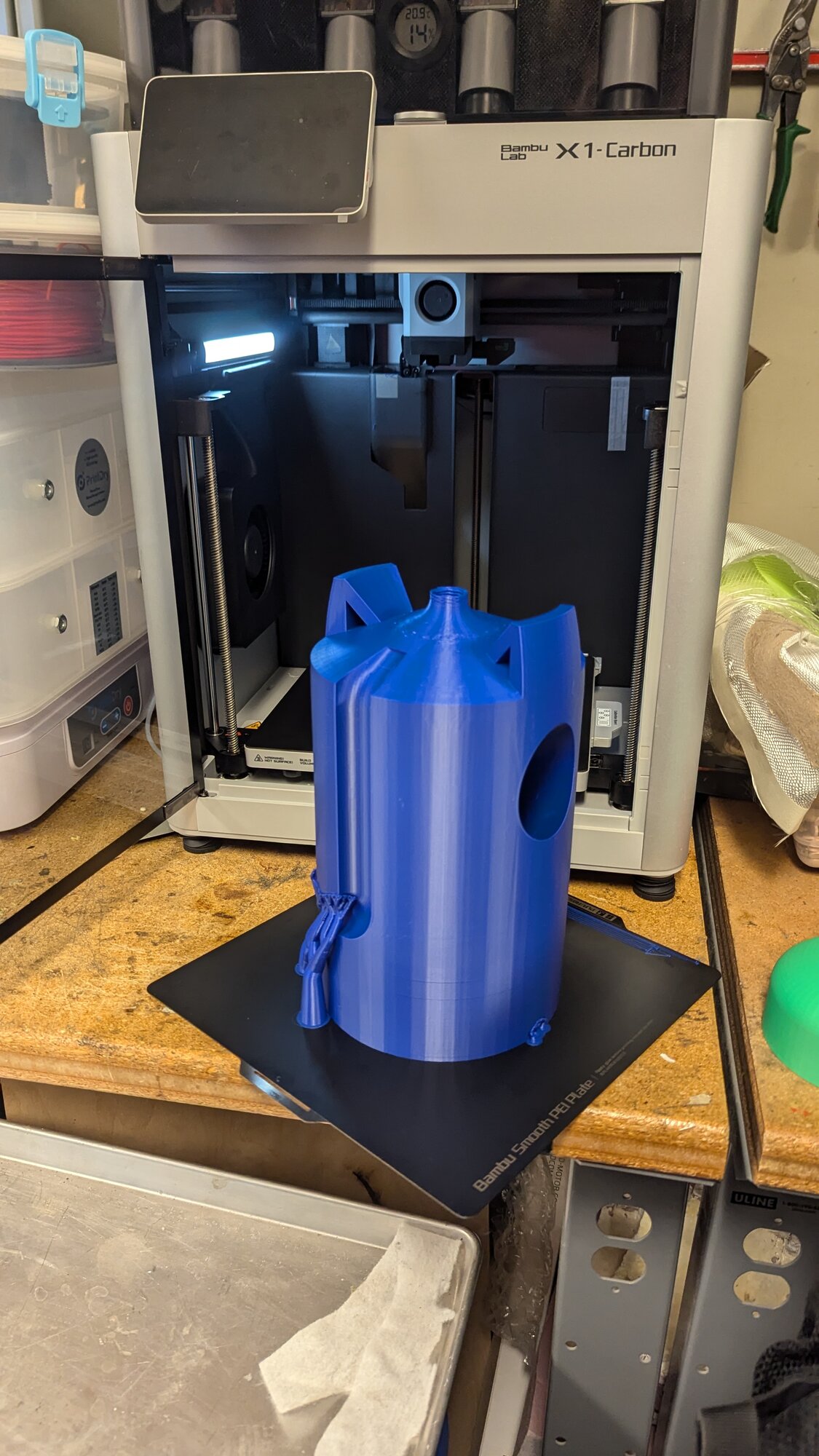 A freshly 3D printed blue payload tank shell sitting on the build plate of a Bambu Lab X1-Carbon printer