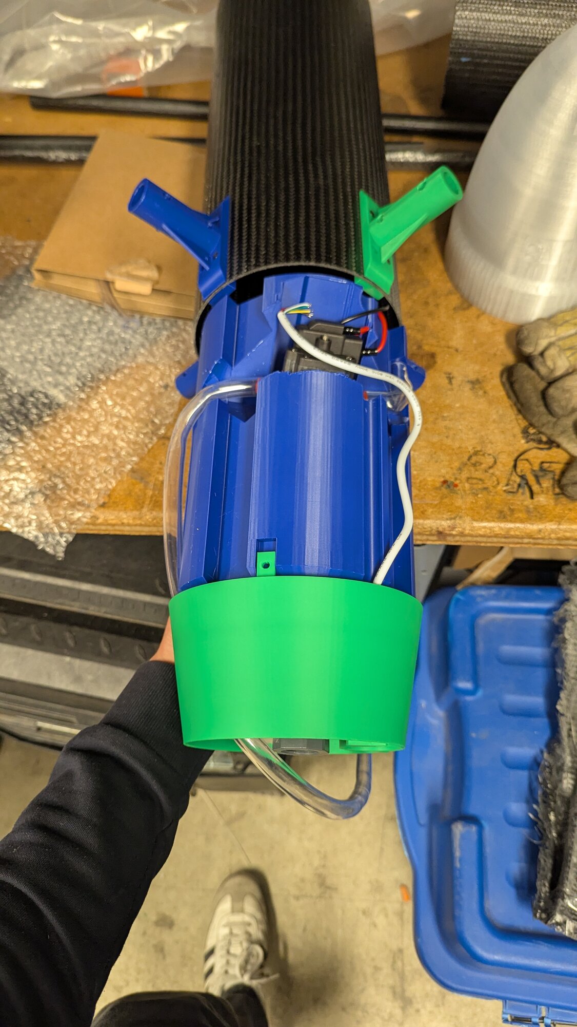 Close-up of the assembled payload tank held in hand, showing the internal wiring and water tube routing near the green mounting ring