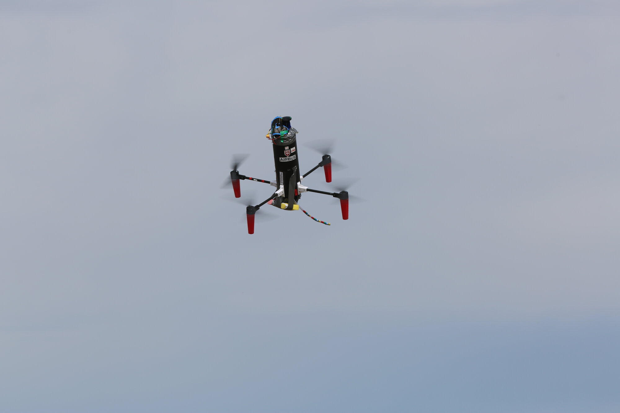 The McGill Aerial Design quadcopter carrying the black payload fuselage in flight against an overcast sky