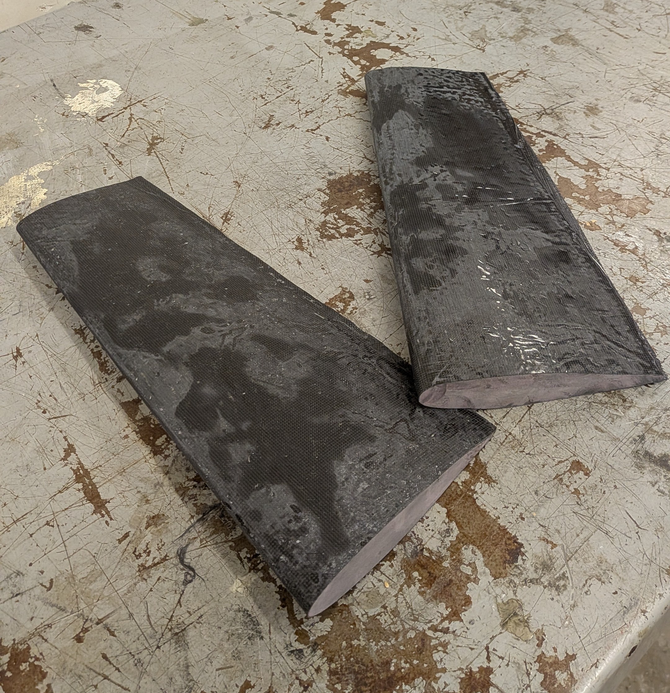 Two carbon fiber tail stabilizer shells sitting on a workbench