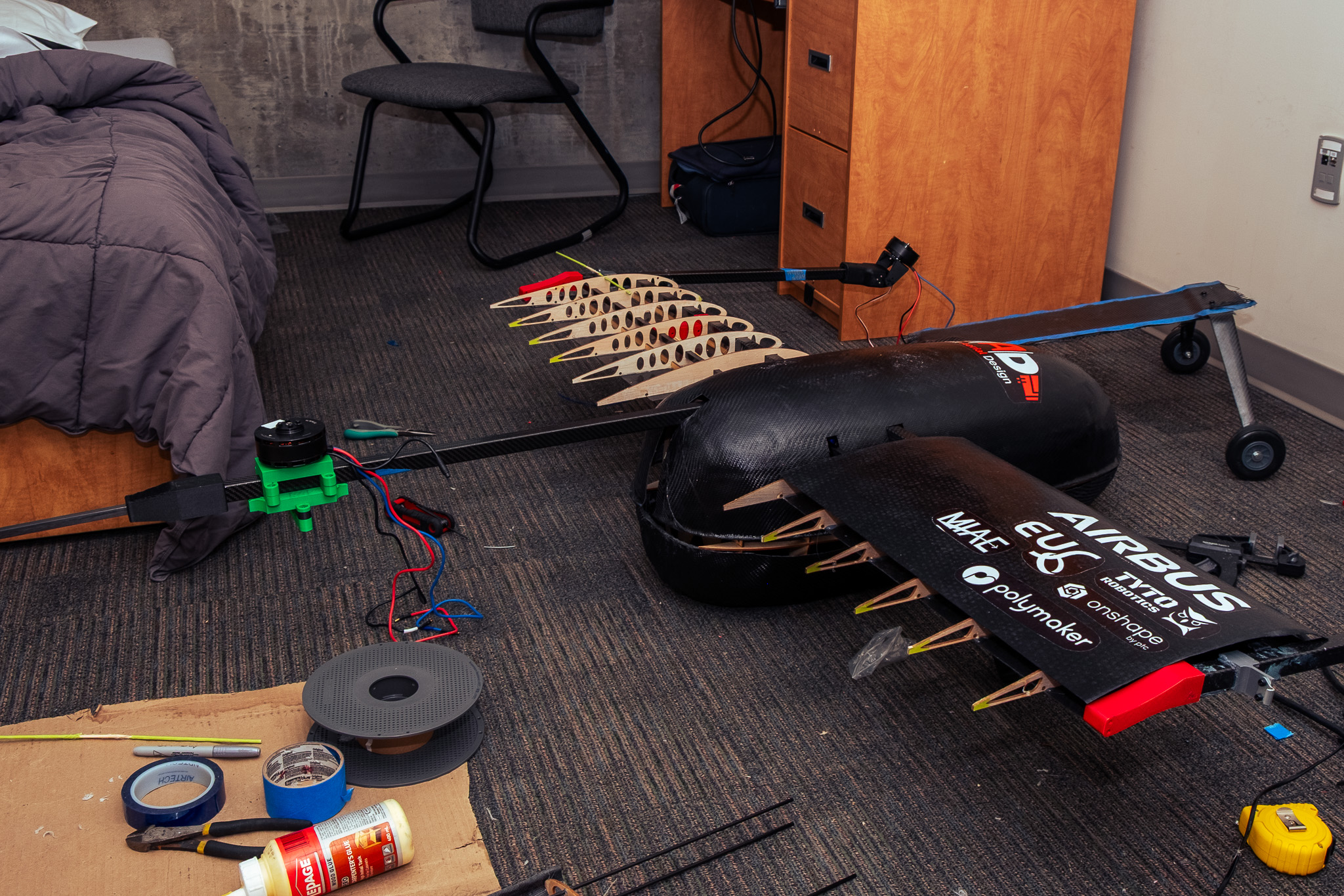 Wing ribs, motor, and fuselage components laid out on a dorm room floor during last-minute competition assembly
